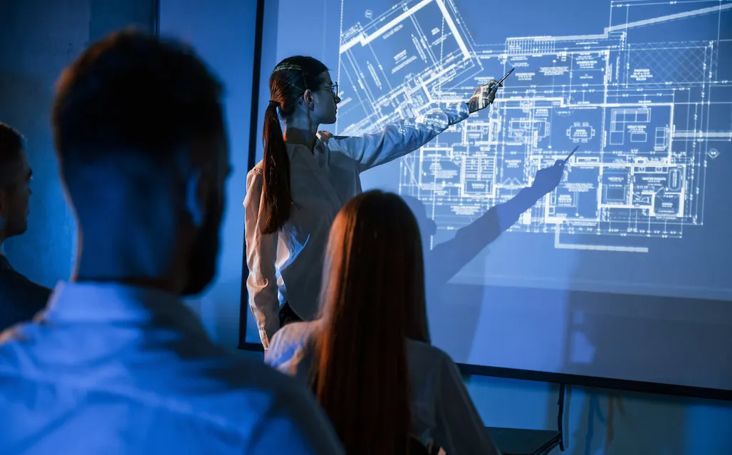 woman pointing to blueprint projected on screen