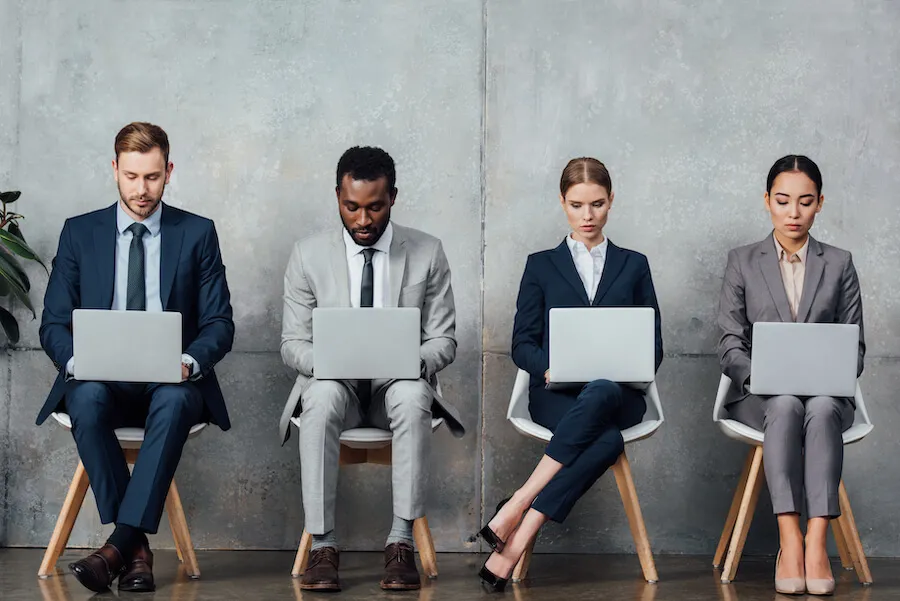 four people on laptops awaiting a job interview